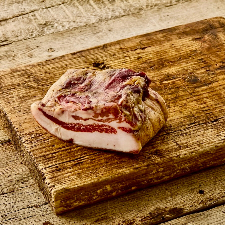 A piece of guanciale on a wooden cutting board, showcasing its fresh, pink color and fatty texture.