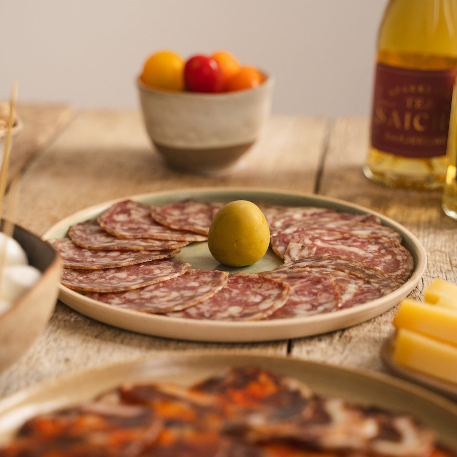 Platter of cured meats with bread, cheese, and fruit on a wooden table.